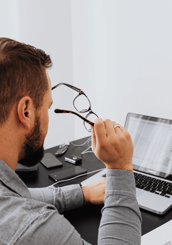 Man holding glasses while reviewing laptop charts